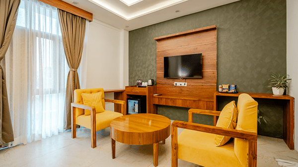 Elegant hotel room seating space with yellow upholstered armchairs, a wooden coffee table, and a wall-mounted TV.