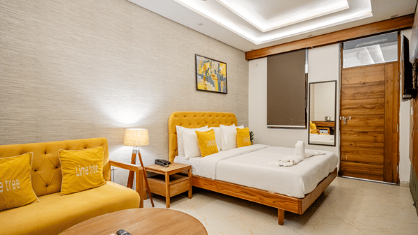 Well-lit hotel guest room displaying a yellow upholstered sofa chair and a double bed.