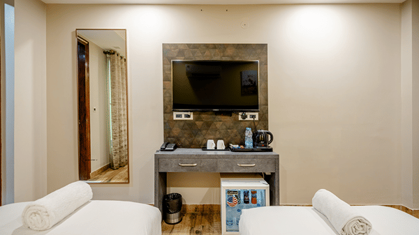 Grey dressing table with a wall-mounted television and a mini-fridge nestled underneath, set between two twin beds.