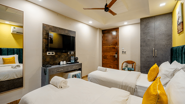 Modern hotel twin room with two single beds, yellow accent cushions, a wall-mounted TV, and wooden flooring.