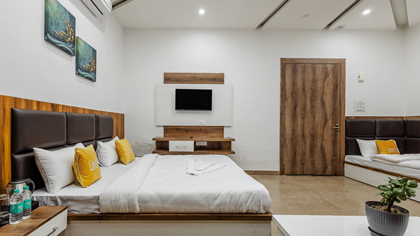 A tidy hotel room showcasing a double bed with yellow cushions, a dark headboard, a wall-mounted TV, and extra beds.