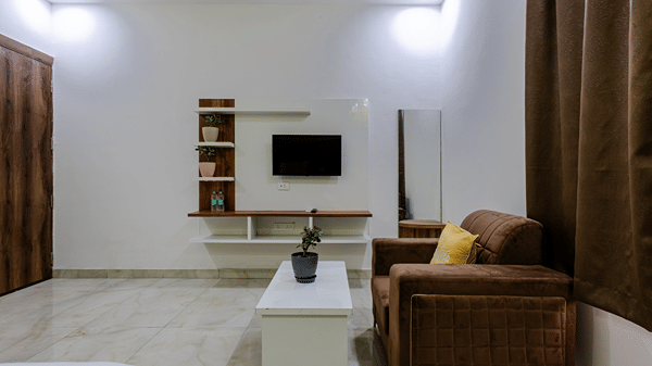 A sleek suite sitting area featuring a brown armchair, a white coffee table, and a wall-mounted flat-screen television.