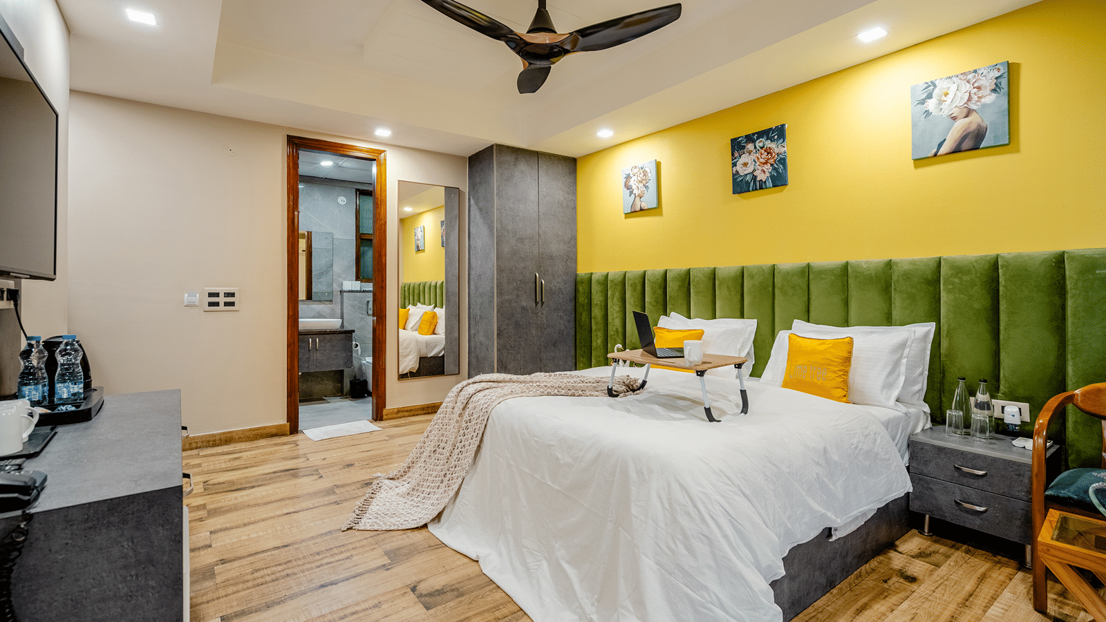 Cosy hotel double bed featuring an open laptop on a portable tray desk, with a wall-mounted TV behind.