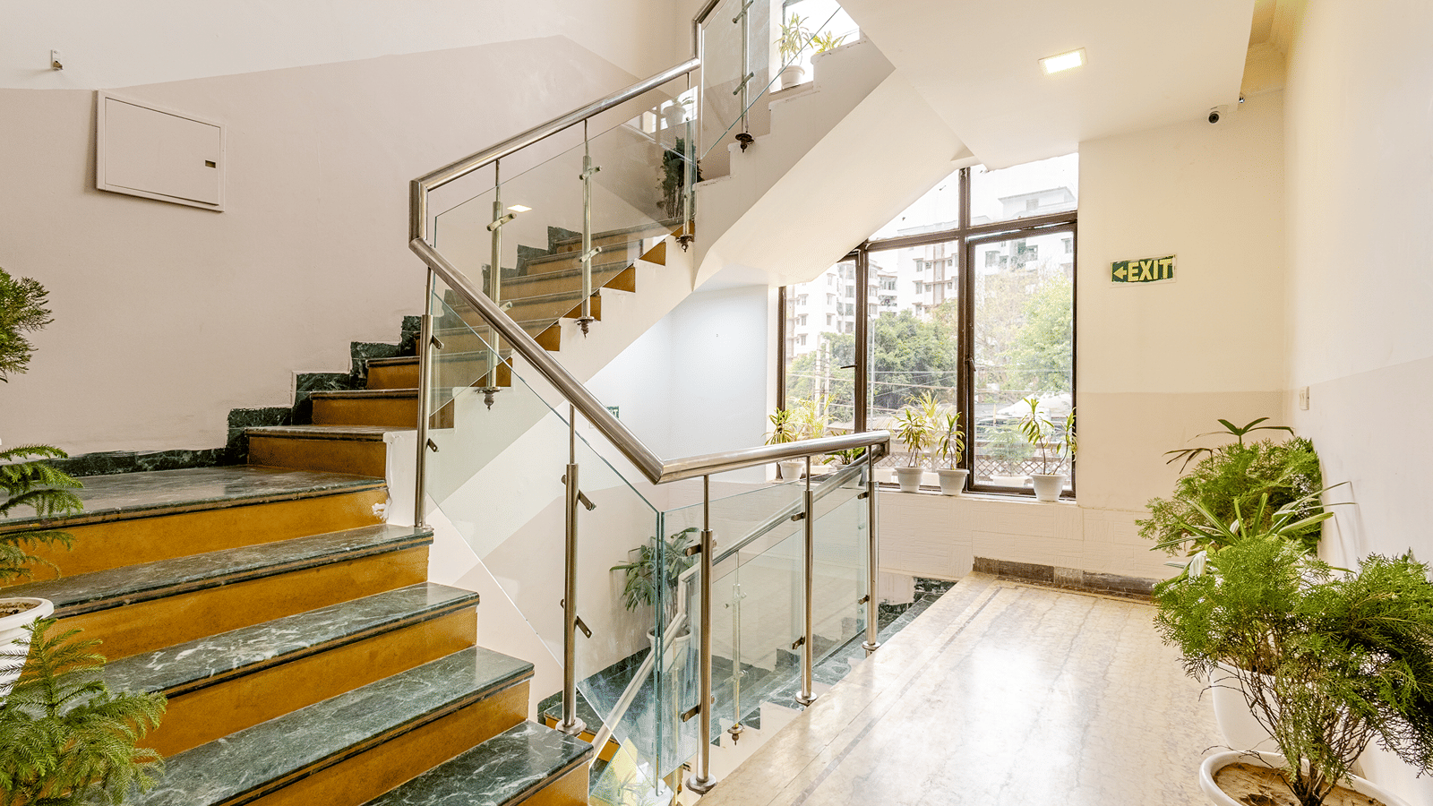 Bright hotel staircase with glass railings and indoor plants.