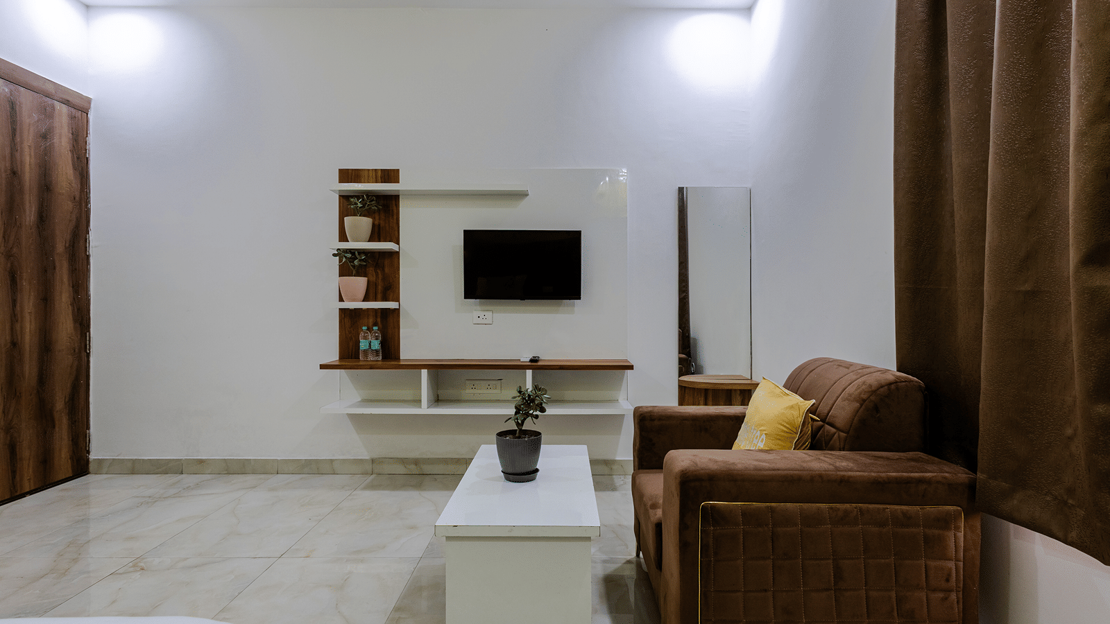 A sleek suite sitting area featuring a brown armchair, a white coffee table, and a wall-mounted flat-screen television.