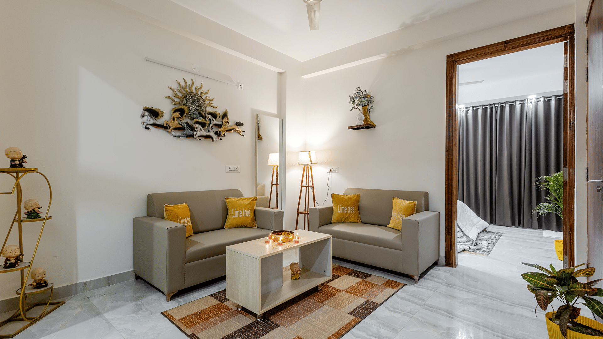 Living room of Lime Tree Hotels & Service Apartment Private Limited featuring a grey sofa, potted plants, and wall decor above a console.