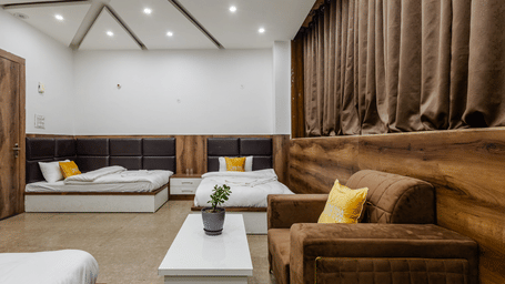 A spacious bedroom suite featuring a brown fabric sofa, a white coffee table, and several beds arranged along the walls.