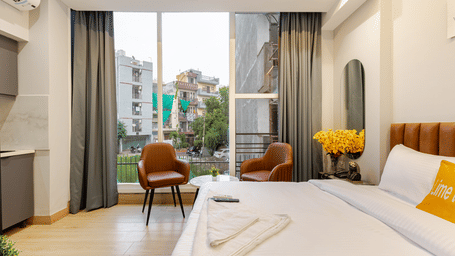 Bedroom of Lime Tree Hotels & Service Apartment Private Limited featuring white bedding, a vase of yellow flowers, and armchairs by the window.