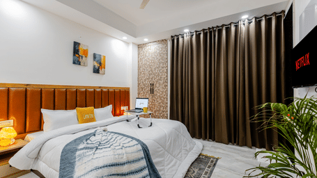 Bedroom of Lime Tree Hotels & Service Apartment Private Limited featuring a wooden panelled headboard, dark curtains, and a study desk.