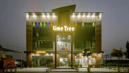 Multiple storey building exterior of Lime Tree Hotels & Service Apartment Private Limited featuring a green illuminated facade at night.