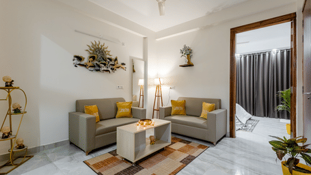 Living room of Lime Tree Hotels & Service Apartment Private Limited featuring a grey sofa, potted plants, and wall decor above a console.