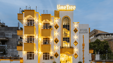 Ornate multiple storey building exterior of Lime Tree Hotels & Service Apartment Private Limited illuminated at dusk with decorative arches.