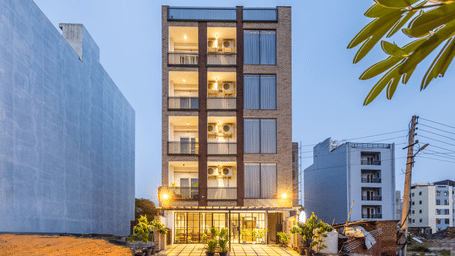 Multiple storey building exterior of Lime Tree Hotels & Service Apartment Private Limited illuminated at dusk with a paved walkway.