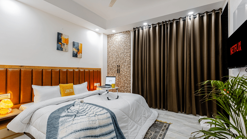 Bedroom of Lime Tree Hotels & Service Apartment Private Limited featuring a wooden panelled headboard, dark curtains, and a study desk.