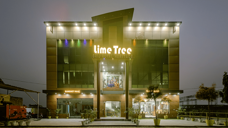 Multiple storey building exterior of Lime Tree Hotels & Service Apartment Private Limited featuring a green illuminated facade at night.