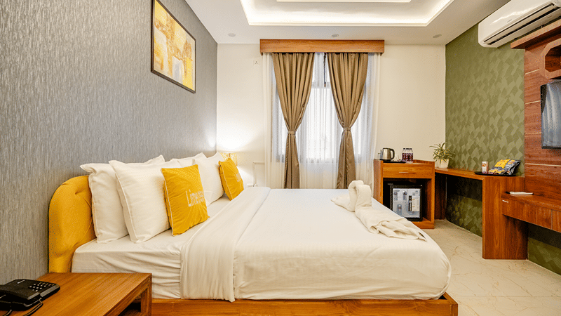 Bedroom of Lime Tree Hotels & Service Apartment Private Limited featuring a bed with yellow cushions, a cove lit ceiling, and curtained windows.