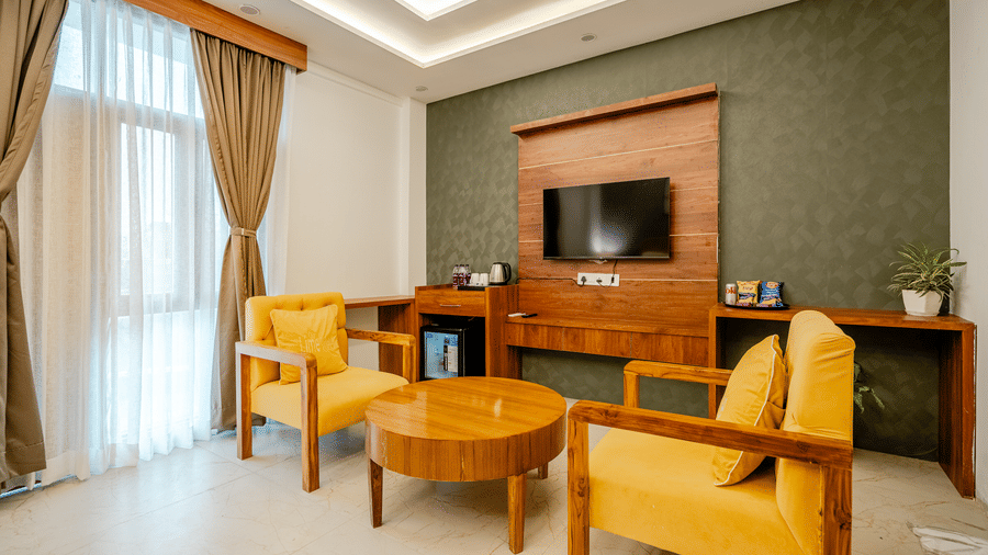 Elegant hotel room seating space with yellow upholstered armchairs, a wooden coffee table, and a wall-mounted TV.