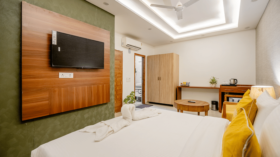 Modern hotel room with a wall-mounted TV on a wooden panel, white bed linen, and a yellow cushion.