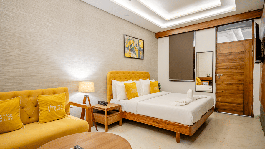 Well-lit hotel guest room displaying a yellow upholstered sofa chair and a double bed.