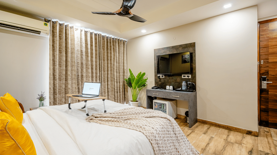 Cosy hotel double bed featuring an open laptop on a portable tray desk, with a wall-mounted TV behind.