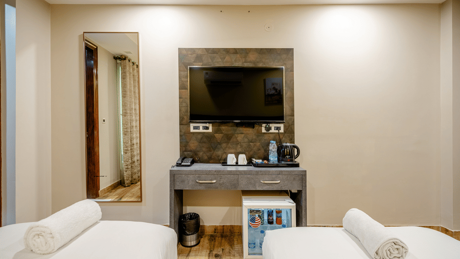 Grey dressing table with a wall-mounted television and a mini-fridge nestled underneath, set between two twin beds.