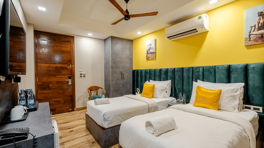 Bright hotel twin bedroom showcasing green tufted headboards, yellow walls, and a wooden entrance door.