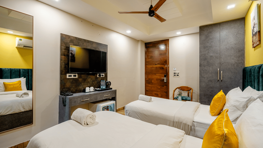 Modern hotel twin room with two single beds, yellow accent cushions, a wall-mounted TV, and wooden flooring.