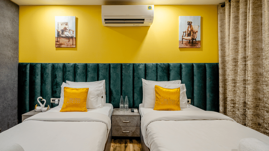 Close-up of twin beds in a hotel room, featuring teal tufted headboards, yellow pillows, and a central bedside table.
