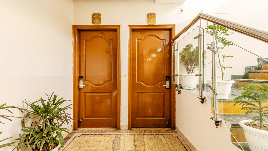 Hotel corridor with  room entrances, staircase, and indoor plants.