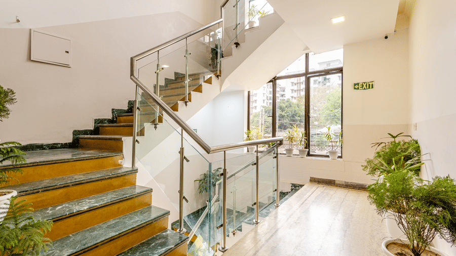Bright hotel staircase with glass railings and indoor plants.