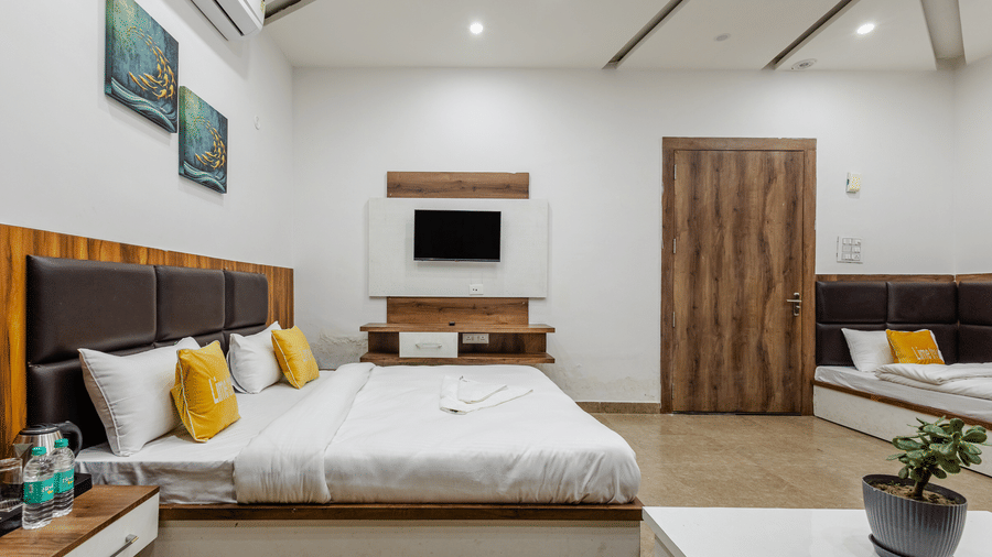 A tidy hotel room showcasing a double bed with yellow cushions, a dark headboard, a wall-mounted TV, and extra beds.