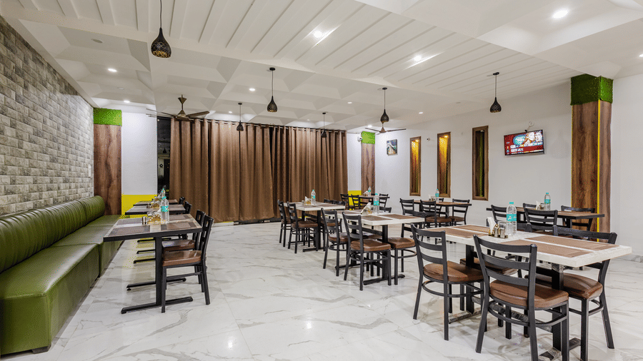 A modern hotel restaurant area with neatly arranged wooden dining tables, dark chairs, and a long green banquette sofa.