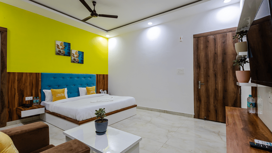 A spacious hotel bedroom with a double bed, a blue headboard, a bright lime green accent wall, and a brown sofa.