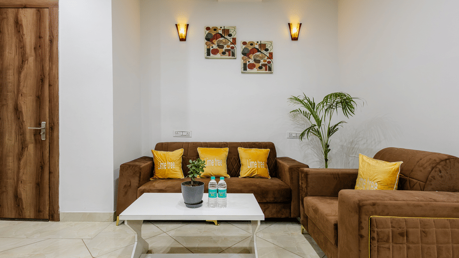 A cosy lounge area inside a hotel suite featuring brown fabric sofas with yellow scatter cushions and a white coffee table.