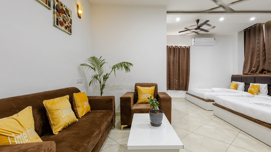 A large hotel suite featuring a brown velvet sofa with yellow cushions, a coffee table, and multiple beds lined up in the background.
