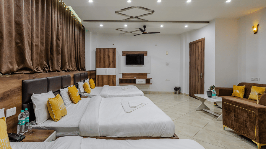 A wide view of a spacious hotel family suite with three double beds, a brown fabric sofa, and full-length curtains.