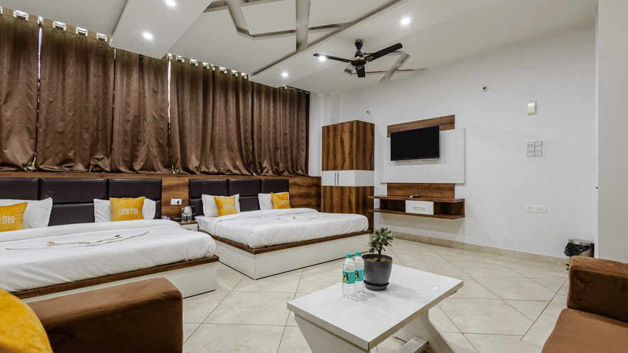 A very spacious family suite featuring multiple neatly made beds, a seating area, and full-length brown curtains.