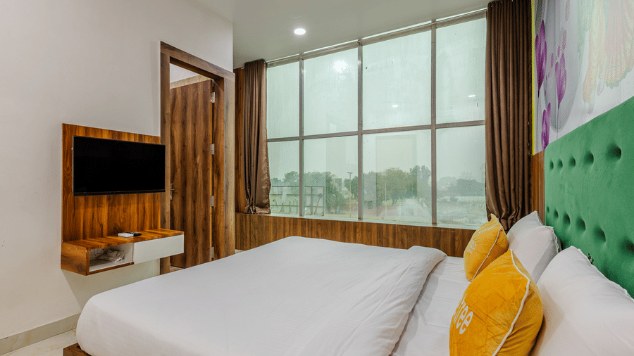 A hotel bedroom featuring a neatly made bed with yellow pillows, a wall-mounted television, and a bright green headboard.