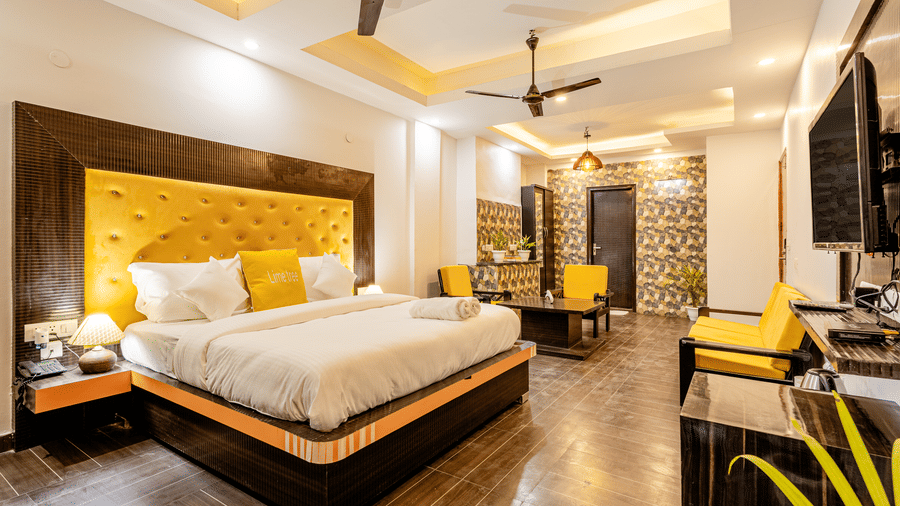 Suite of Lime Tree Hotels & Service Apartment Private Limited featuring a yellow padded headboard, a bed, and a seating area.