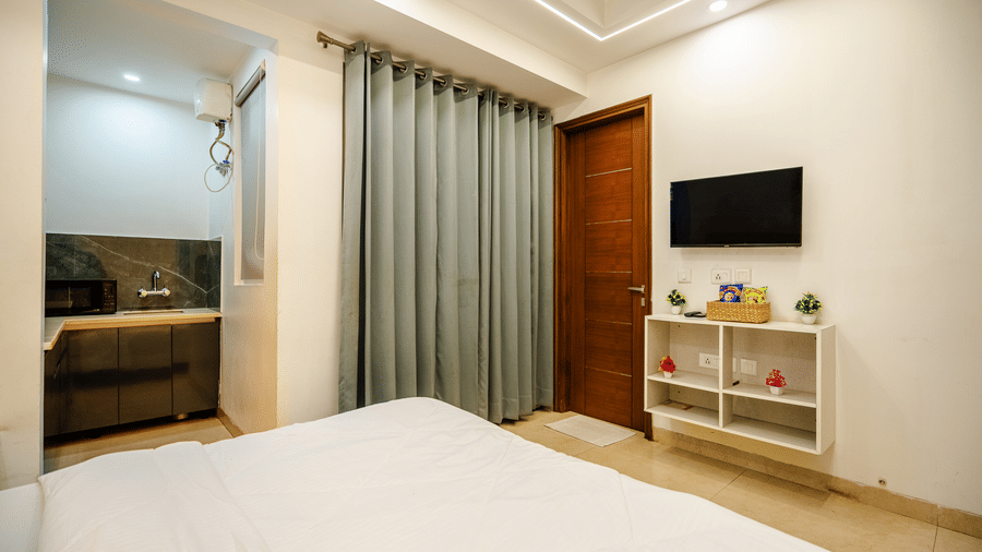 Bedroom of Lime Tree Luxury Studio featuring a wall mounted television, a console, and grey curtains.