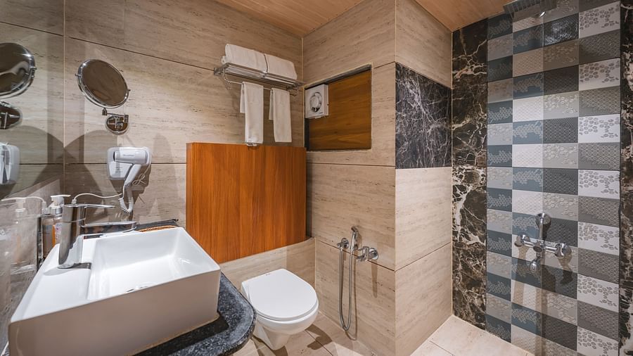 A well-lit bathroom features a modern sink, a toilet, and a shower area with patterned tiling - Lords Eco Inn Ambaji.