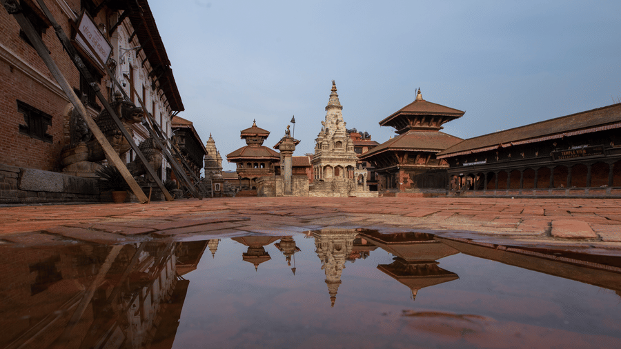 A facade view of the bhaktapur durbar square where a puddle of water is reflecting the structure