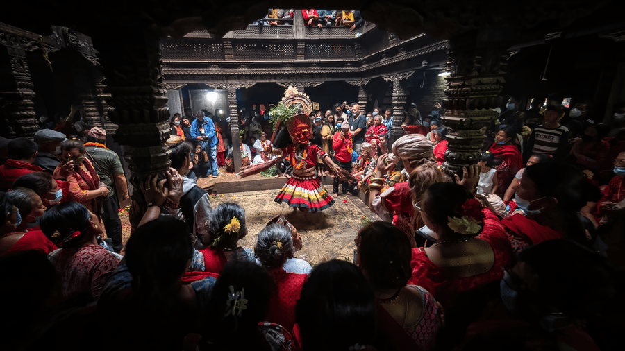 An atmospheric evening view of a traditional Lakhey dance performance inside a historic brick palace courtyard in Bhaktapur, Nepal.