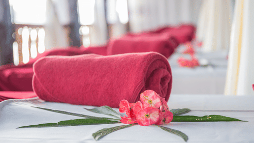 Rolled red towels arranged on a spa bed with pink flower petals