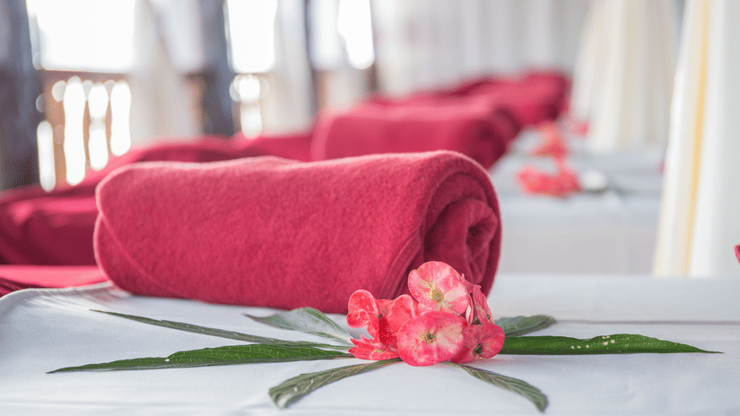 Rolled red towels arranged on a spa bed with pink flower petals