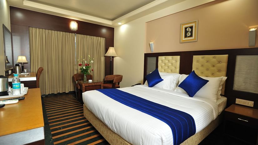 Hotel Dr Rajkumar International offers a premium room with a king-size bed, elegant lighting, and modern decor