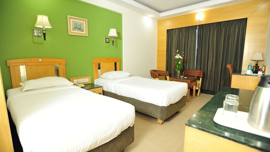 Twin-bed room with green accent wall, wooden furniture, and bright lighting at Hotel Dr Rajkumar International.
