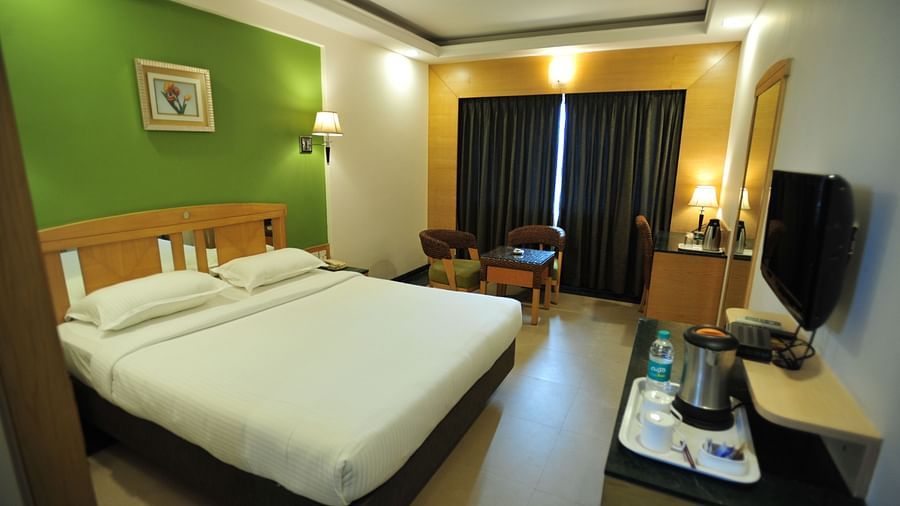 King size room with soft lighting, cosy decor, and Pair of chair and a round table placed near the curtains at Hotel Dr Rajkumar International.
