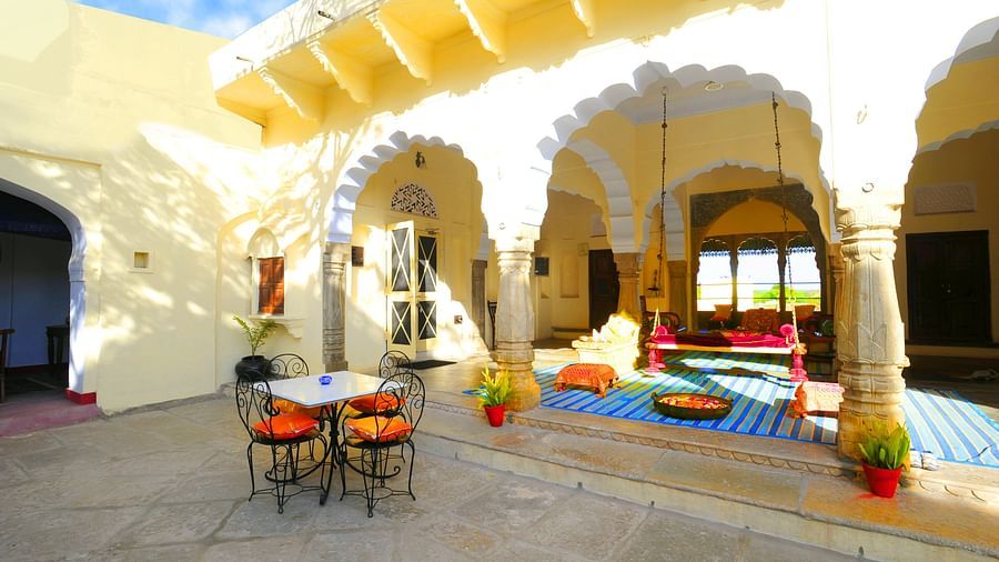 A sun-drenched courtyard at Fort Barli, with arched colonnades and a swing, offers a charming blend of architecture and relaxation.