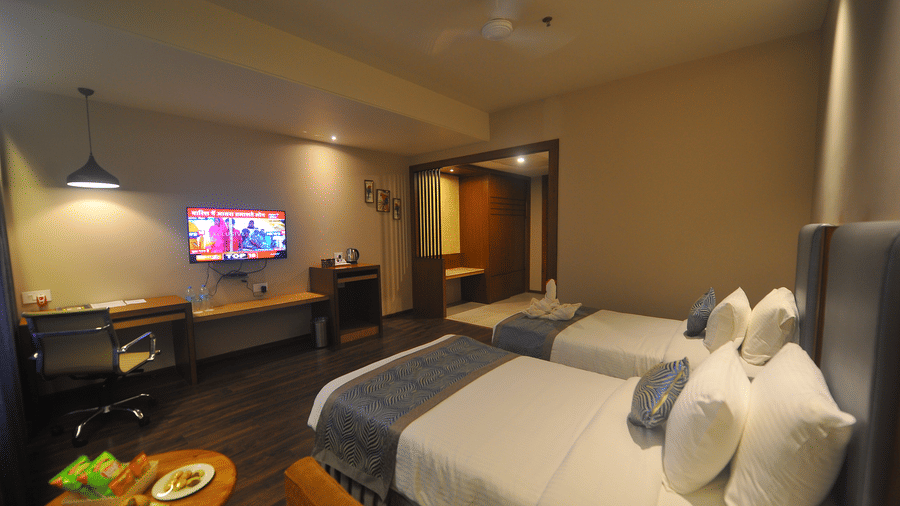 Twin bed hotel room with dark wooden flooring, a wall-mounted television, long blue curtains and a breakfast tray placed on a low round table.